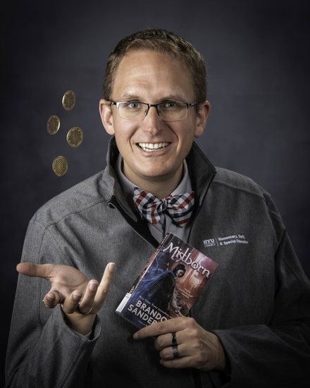 Benjamin Pacini, smiling, tossing coins and holding a copy of Mistborn